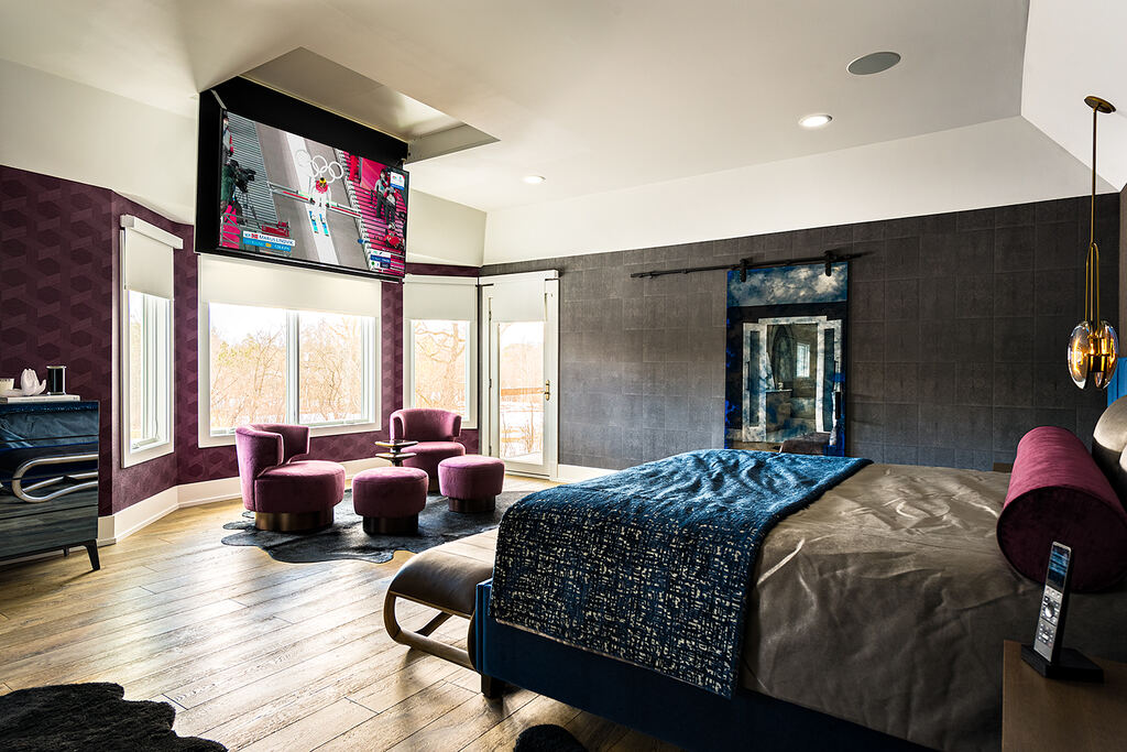 Bedroom with a wall-mounted display, upholstered bed, lounge chairs, and windows