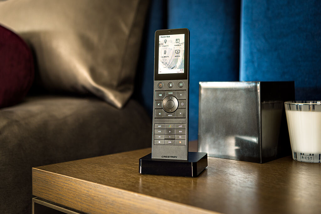 Handheld control resting on a bedside table beside an upholstered bed